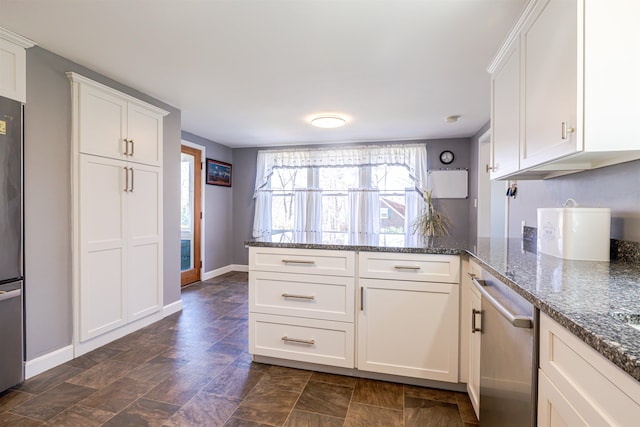 kitchen with a peninsula, white cabinets, dark stone countertops, and baseboards