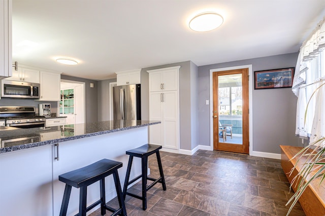 kitchen featuring stainless steel appliances, baseboards, a breakfast bar, stone finish flooring, and white cabinets