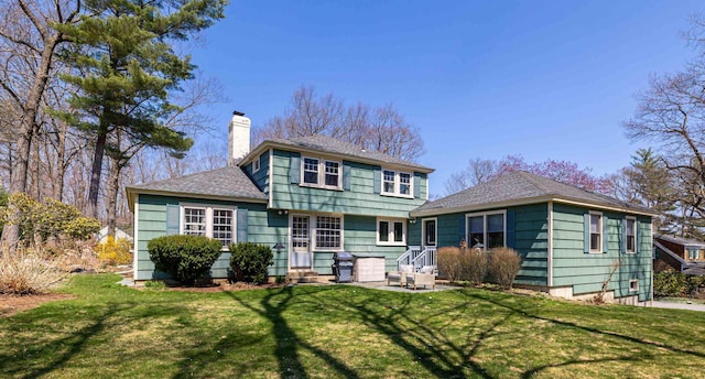 back of property with a shingled roof, a chimney, and a yard