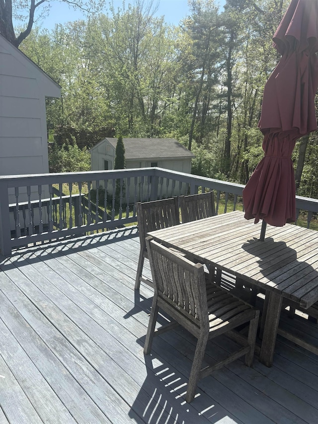 wooden deck with an outdoor structure, outdoor dining space, and a storage unit