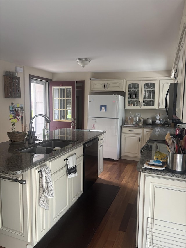 kitchen with a sink, black dishwasher, freestanding refrigerator, glass insert cabinets, and dark wood-type flooring