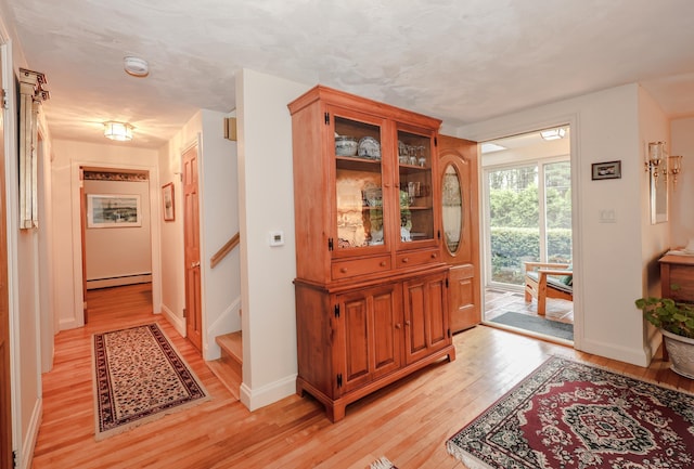 corridor featuring a baseboard heating unit, light wood-style floors, baseboards, and stairs
