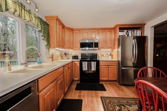 kitchen featuring stainless steel appliances, a sink, light countertops, and light wood finished floors