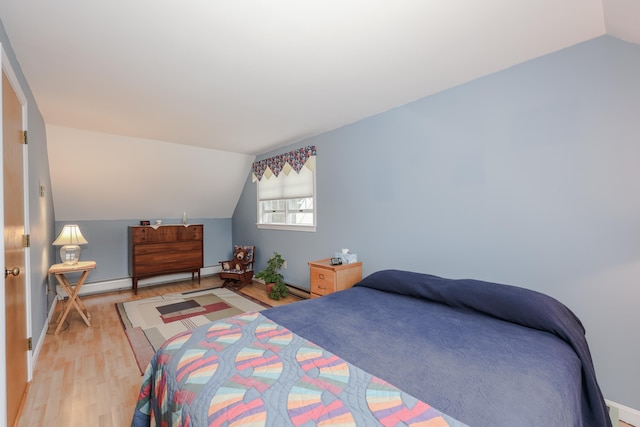 bedroom with lofted ceiling, light wood finished floors, a baseboard heating unit, and baseboards
