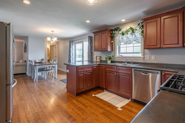 kitchen with appliances with stainless steel finishes, a sink, dark countertops, a chandelier, and a peninsula