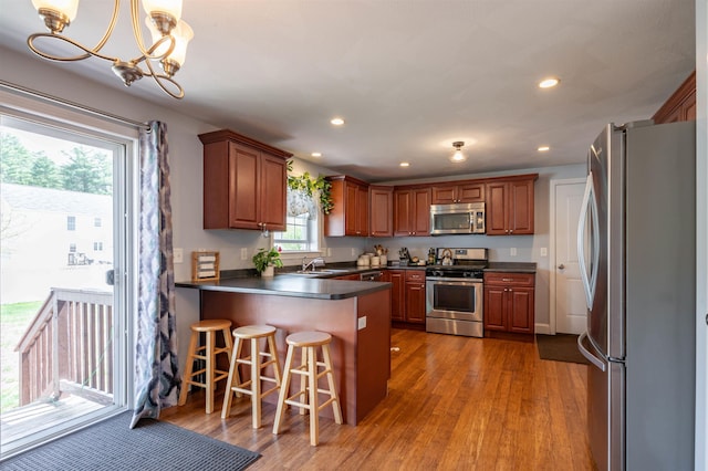 kitchen featuring stainless steel appliances, dark countertops, a peninsula, a sink, and wood finished floors