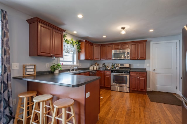 kitchen with stainless steel appliances, dark countertops, a sink, a peninsula, and wood finished floors