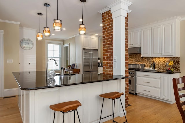 kitchen with appliances with stainless steel finishes, a sink, under cabinet range hood, tasteful backsplash, and dark countertops
