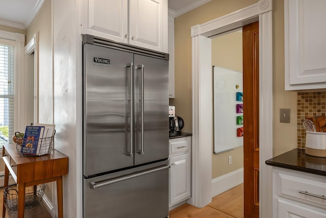 kitchen with built in refrigerator, crown molding, backsplash, white cabinetry, and healthy amount of natural light