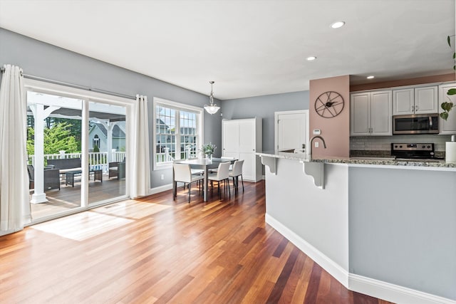 kitchen featuring appliances with stainless steel finishes, recessed lighting, light stone countertops, wood finished floors, and decorative backsplash