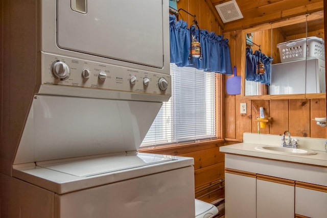 clothes washing area featuring stacked washer / dryer and wooden walls