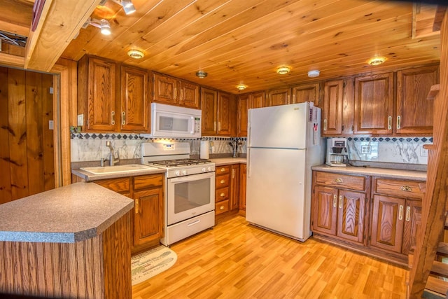 kitchen featuring white appliances, brown cabinetry, backsplash, light wood-type flooring, and a sink