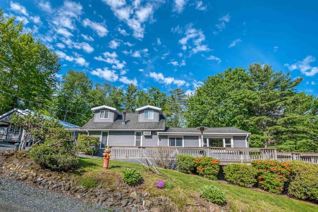 view of front of property featuring a front yard, a wooden deck, and a shingled roof