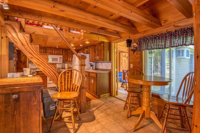 dining space featuring wood ceiling, beam ceiling, light flooring, and wood walls