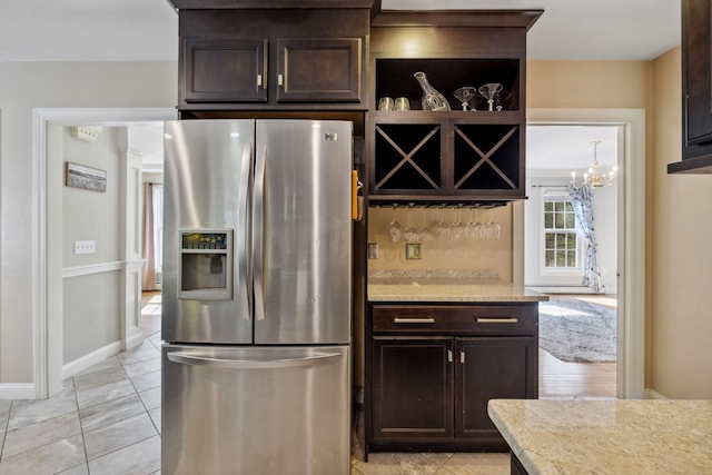kitchen with stainless steel fridge with ice dispenser, dark brown cabinetry, a chandelier, baseboards, and light stone countertops