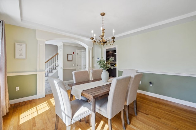 dining area featuring arched walkways, a chandelier, light wood finished floors, stairs, and a tray ceiling