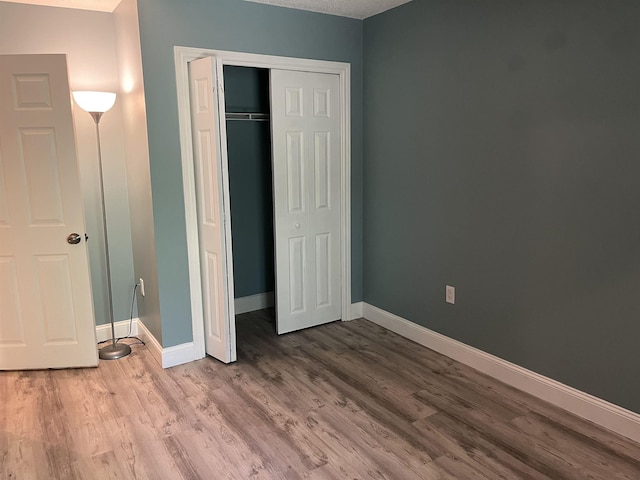 unfurnished bedroom with baseboards, wood finished floors, and a closet