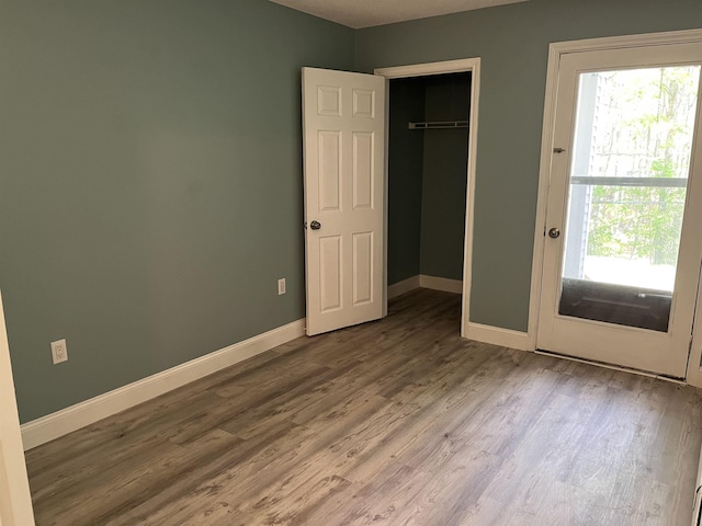 unfurnished bedroom with wood finished floors, baseboards, multiple windows, and a closet