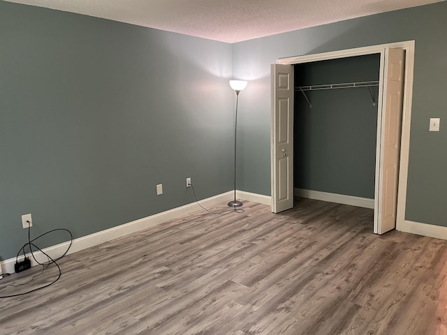 unfurnished bedroom with a textured ceiling, wood finished floors, baseboards, and a closet