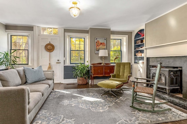 living area with ornamental molding, a wood stove, wood finished floors, and baseboards