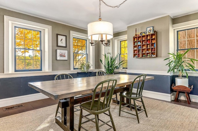 dining room with baseboards, wood finished floors, healthy amount of natural light, ornamental molding, and a chandelier