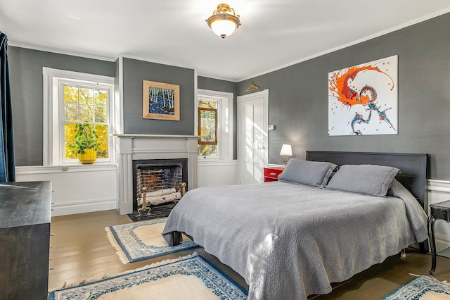 bedroom featuring multiple windows, a fireplace with flush hearth, wood finished floors, crown molding, and baseboards
