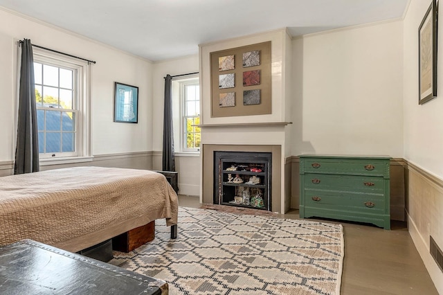 bedroom with a wainscoted wall, crown molding, multiple windows, and a fireplace with flush hearth