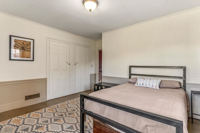 bedroom featuring ornamental molding, wainscoting, wood finished floors, and a closet