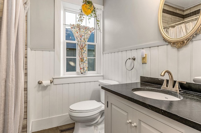 full bathroom featuring a wainscoted wall, toilet, vanity, and a decorative wall