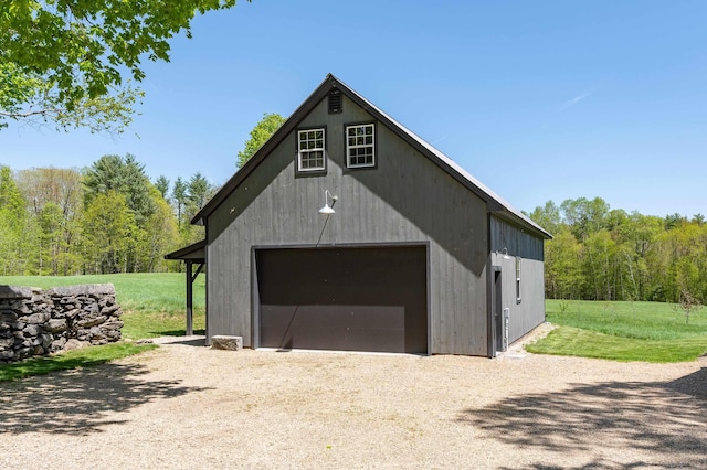 detached garage with gravel driveway and a view of trees