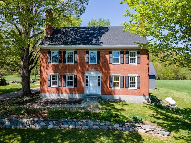 colonial inspired home with a chimney, a front lawn, brick siding, and roof with shingles