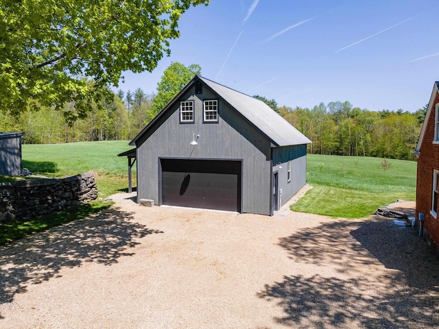 detached garage featuring dirt driveway and a wooded view