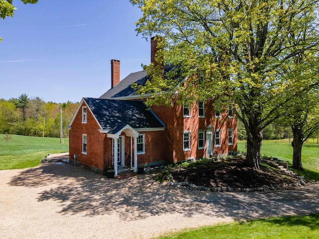 view of side of home featuring a chimney, a lawn, brick siding, and driveway