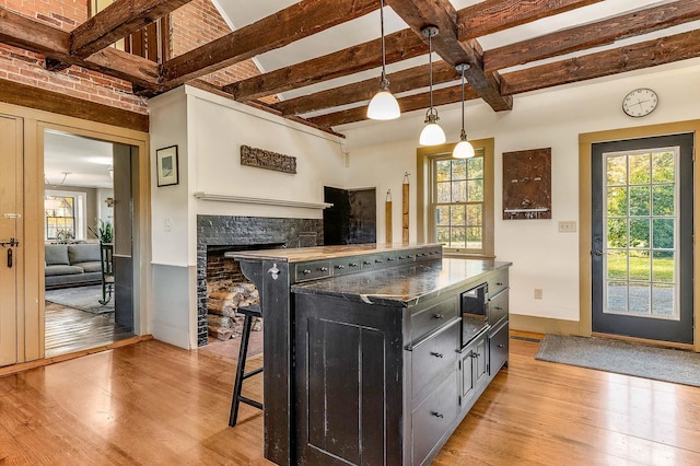 kitchen featuring light wood-type flooring, dark cabinetry, plenty of natural light, and beam ceiling