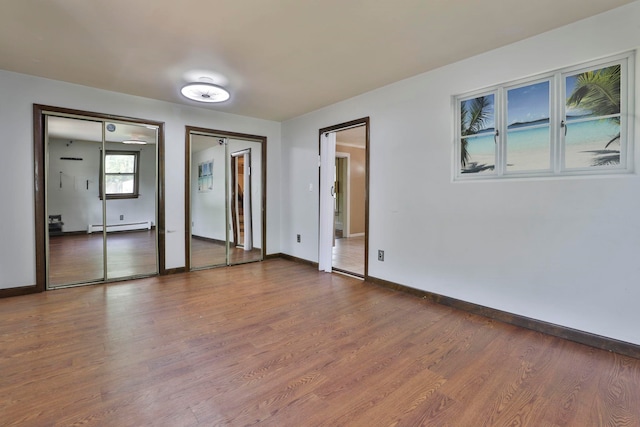 unfurnished bedroom featuring baseboard heating, dark wood finished floors, baseboards, and two closets