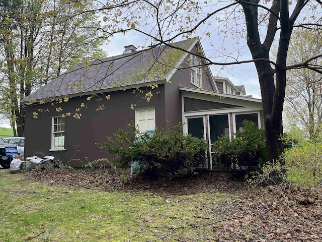 view of side of home with a chimney, stucco siding, and a sunroom