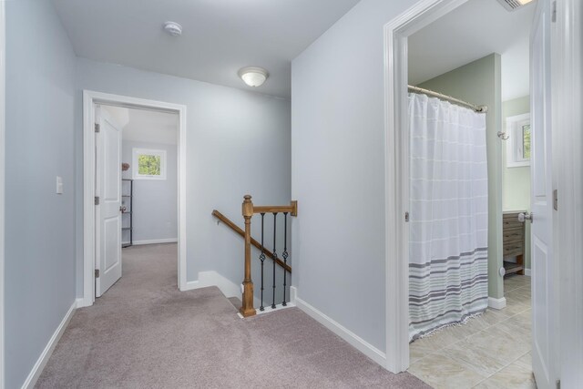 corridor with an upstairs landing, baseboards, and light carpet