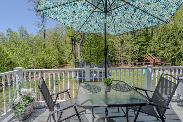 wooden terrace with a trampoline, a playground, outdoor dining area, and a lawn