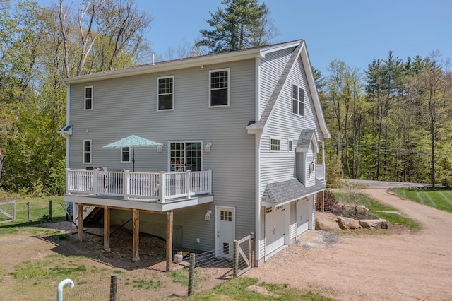rear view of house with an attached garage, a wooden deck, fence, driveway, and a gate