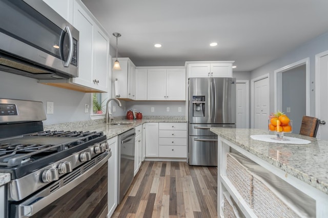 kitchen featuring stainless steel appliances, a sink, white cabinets, wood finished floors, and light stone countertops