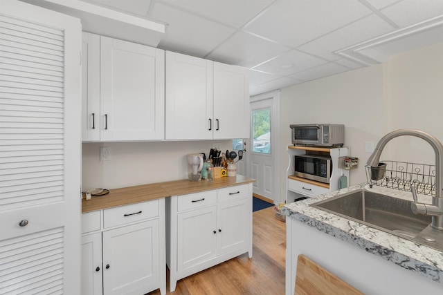 74 Pine St, Rollinsford, NH 03869 - kitchen with a sink, stainless steel microwave, white cabinetry, a paneled ceiling, and light wood finished floors