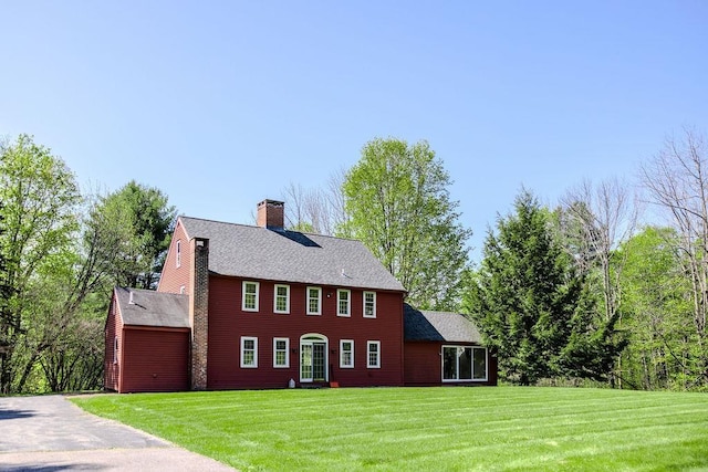 colonial home featuring a front yard, a chimney, and a shingled roof