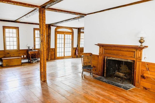 living room featuring a wainscoted wall, light wood-style floors, a fireplace with flush hearth, and wood walls