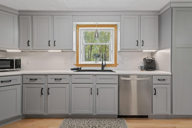 kitchen featuring stainless steel appliances, a sink, gray cabinetry, and tasteful backsplash