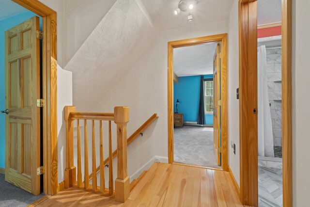 corridor with an upstairs landing, wood finished floors, baseboards, and lofted ceiling