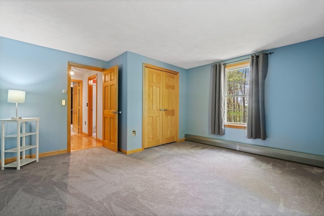 unfurnished bedroom featuring carpet flooring, baseboards, a baseboard radiator, and a closet