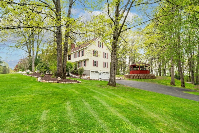 view of home's exterior with driveway, an attached garage, a chimney, and a yard