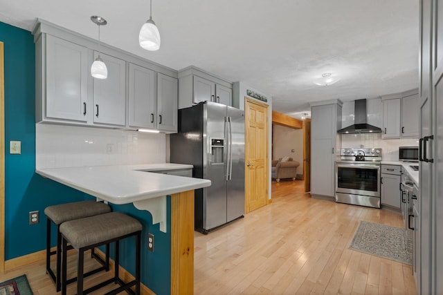 kitchen featuring appliances with stainless steel finishes, wall chimney range hood, gray cabinetry, decorative backsplash, and a kitchen bar