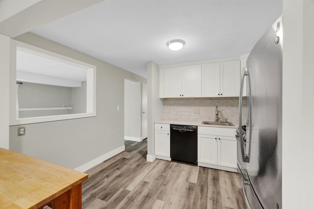 kitchen with dishwasher, a sink, freestanding refrigerator, decorative backsplash, and light wood finished floors