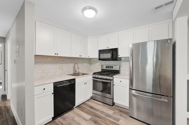 kitchen featuring black appliances, a sink, light wood-type flooring, white cabinets, and a textured ceiling